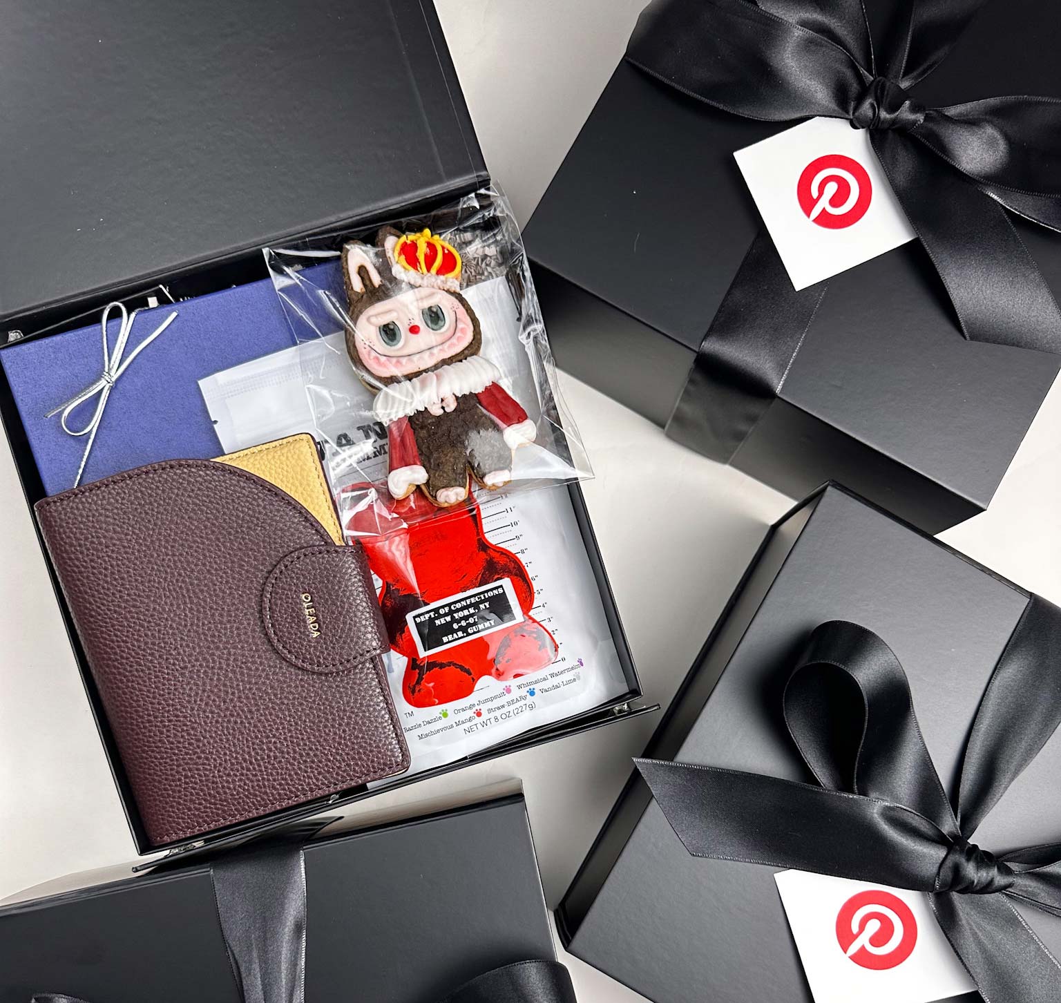 Open gift box with a leather wallet, cookie and stationery items on a white background.