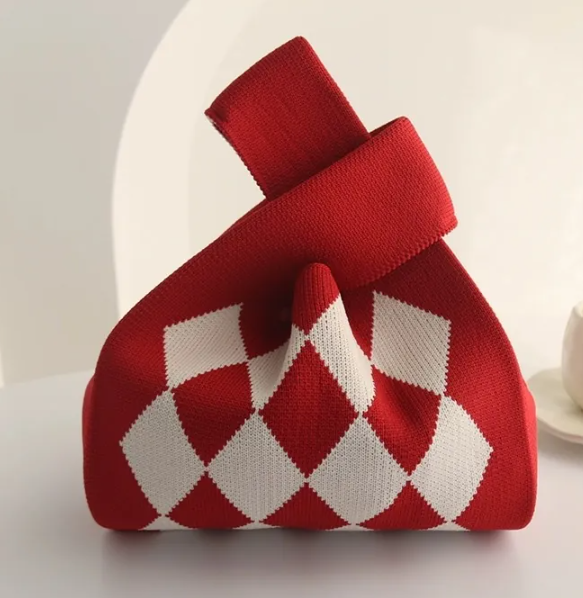 A red and white argyle knit gift bag with a loop handle, photographed on a clean white surface with a soft, minimalist background.