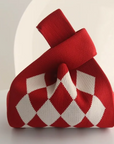 A red and white argyle knit gift bag with a loop handle, photographed on a clean white surface with a soft, minimalist background.