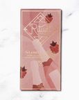 A single bar of Ritual The Apres chocolates in its dusty pink and rose gold packaging with gold foil details and illustrations of rasberries and wine bottles, set against a white marble background.