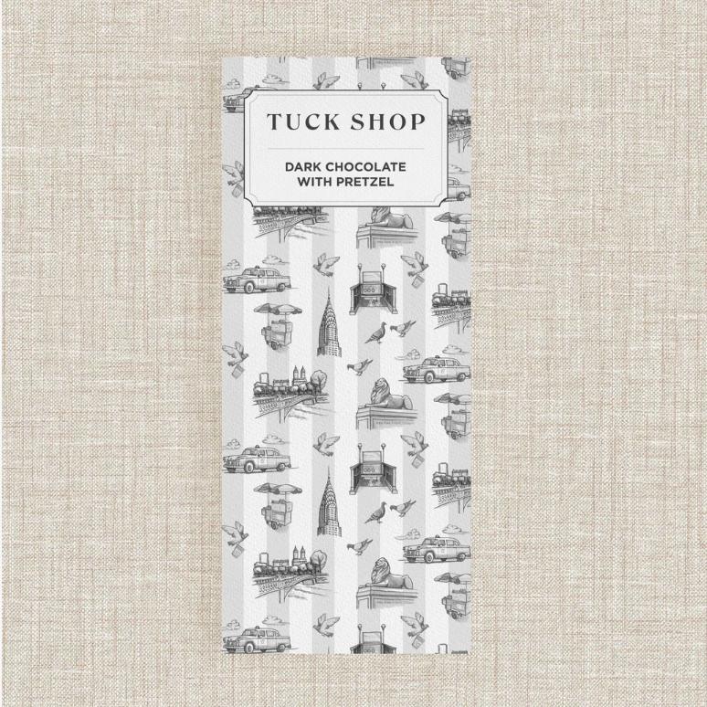 A bar of Tuck Shop Dark Chocolate bar in a white and gray striped packaging featuring black line-art illustrations of London landmarks on a textured beige background.