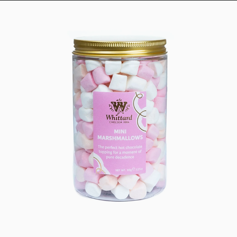 A clear plastic jar filled topped with a gold metal lid with pink and white mini marshmallows, featuring a pink label for Whittard of Chelsea 1954.