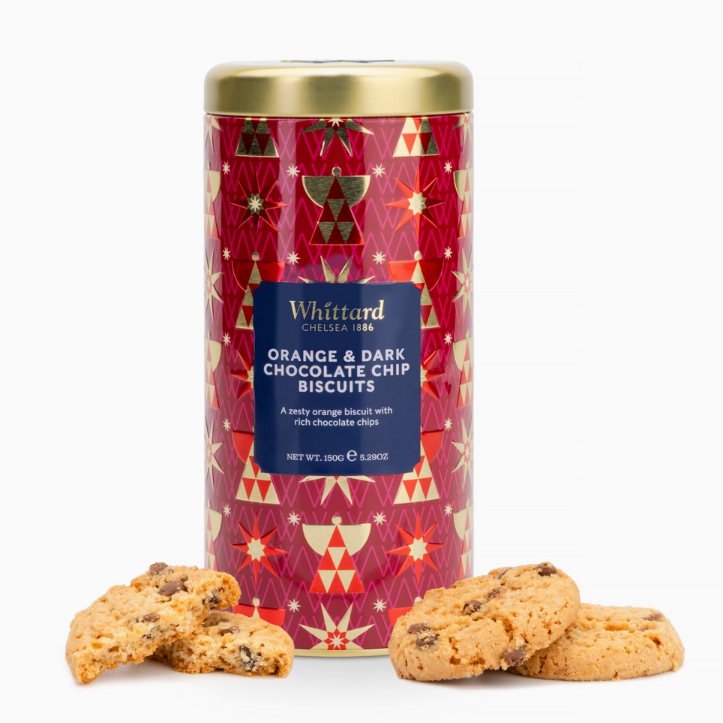 A cylindrical tin of Whittard Orange &amp; Dark Chocolate Chip Biscuits on a white background, with several golden-brown chocolate chip cookies placed in front of the tin.