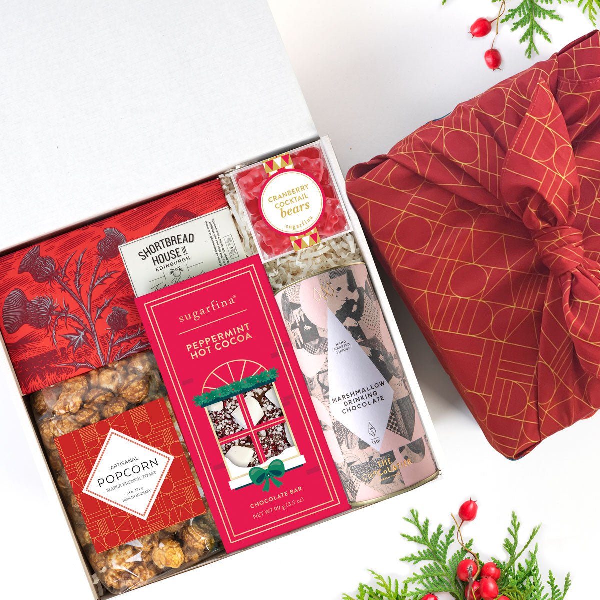 kadoo festive holiday gift box with eco-friendly furoshiki wrap. Gifts: chocolate, popcorn, hot coco, cookies, gummy bears & more.