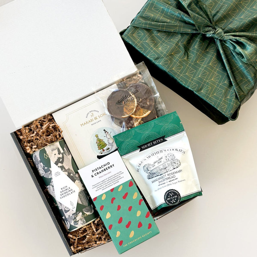 kadoo hot chocolate curated holiday gift box with drinking chocolate, bar of chocolate, shortbread cookies, chocolate orange slice, and more. wrapped in reusable furoshiki fabric.
